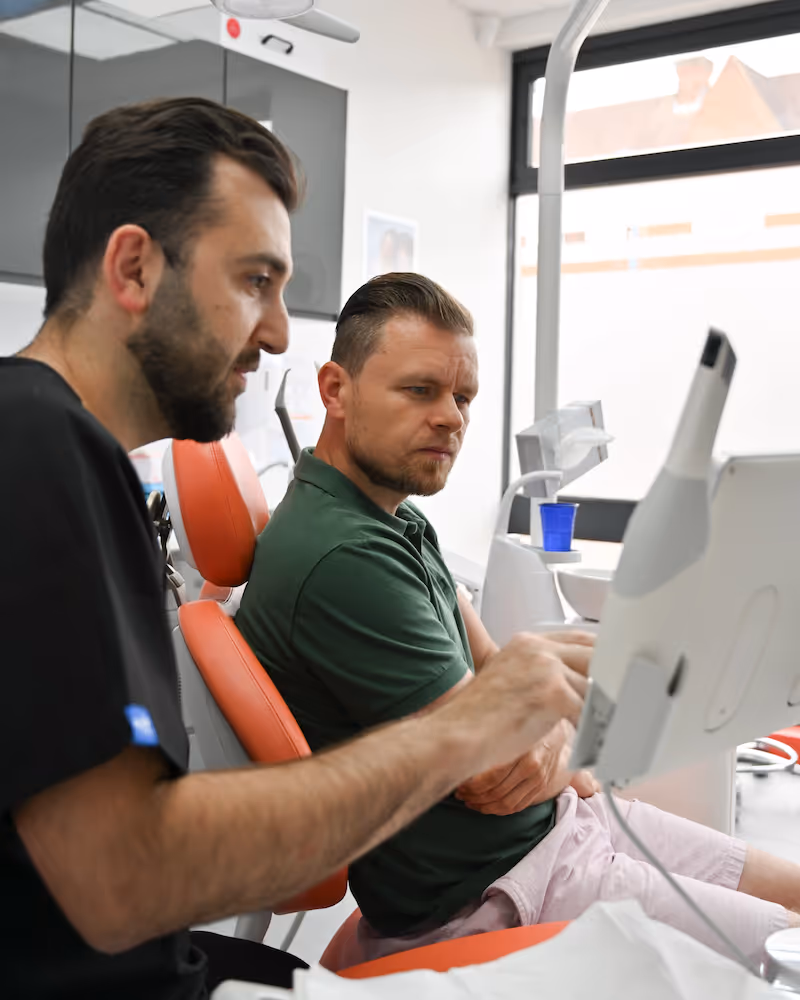 A dentist showing information on a screen to a man seated in a dental chair.