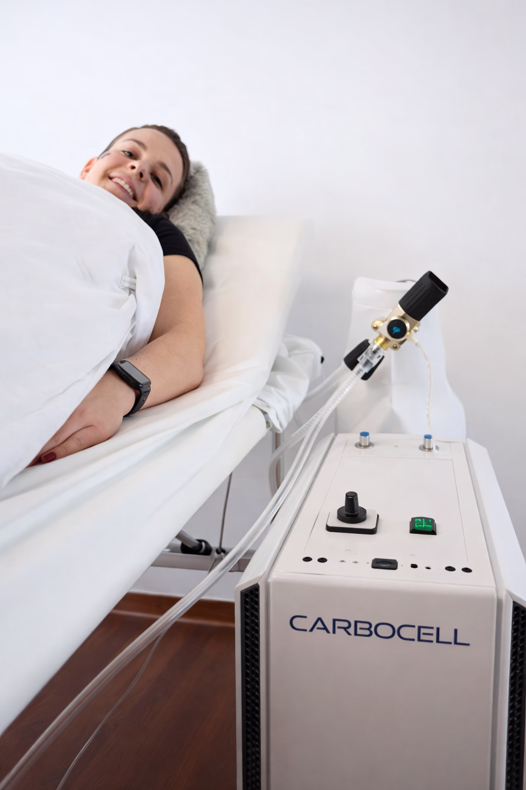 Smiling woman lying on a white medical bed next to a CARBOCELL therapy machine.