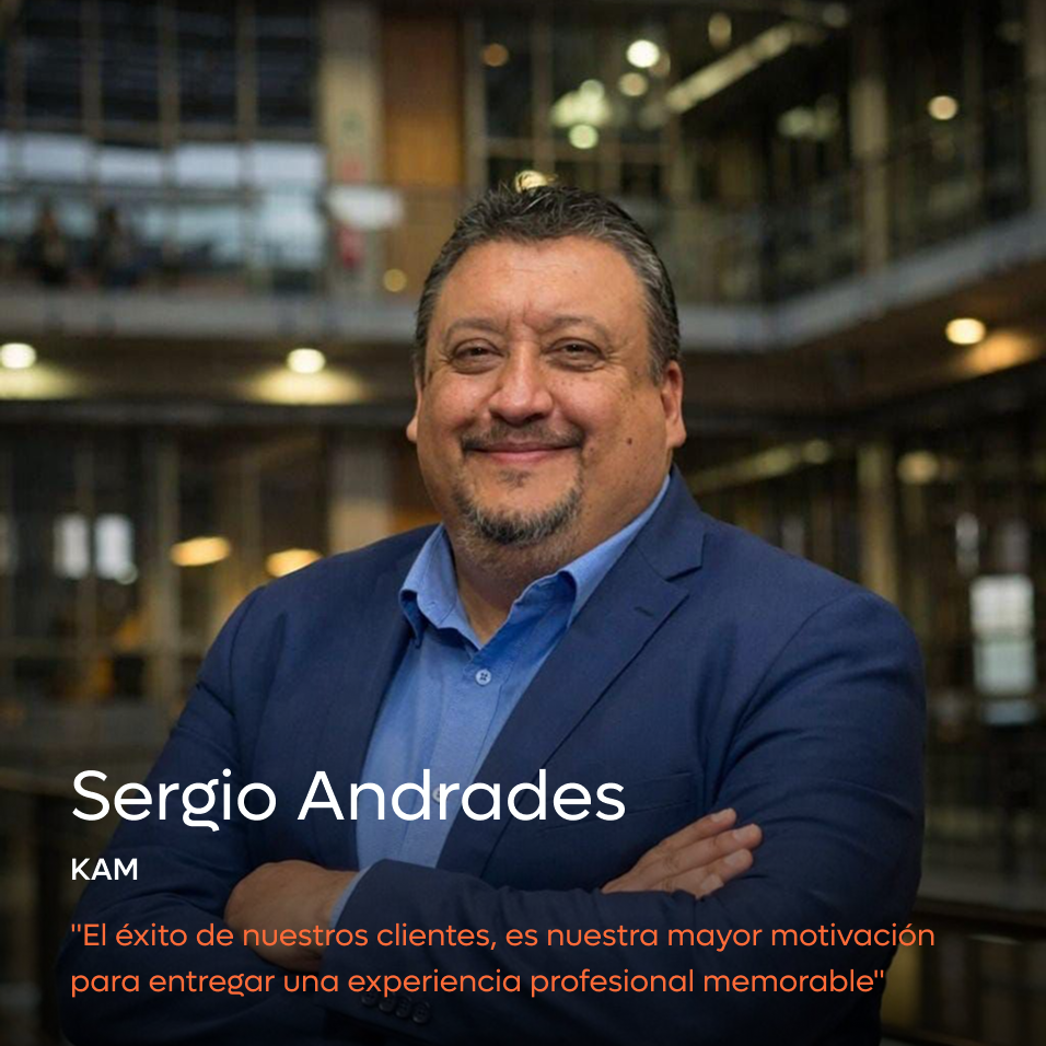 Smiling man with folded arms wearing a blue suit jacket and shirt standing in a modern office building.