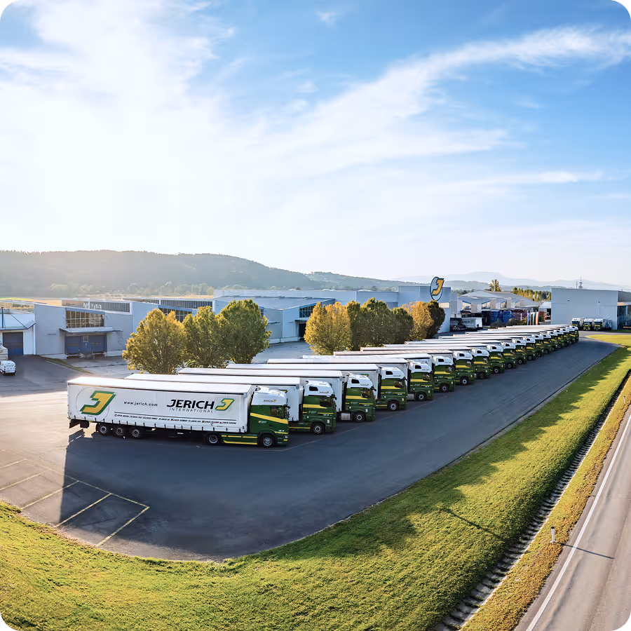 Fleet of Jerich International trucks lined up outside a large warehouse under a clear sky with distant hills in the background.
