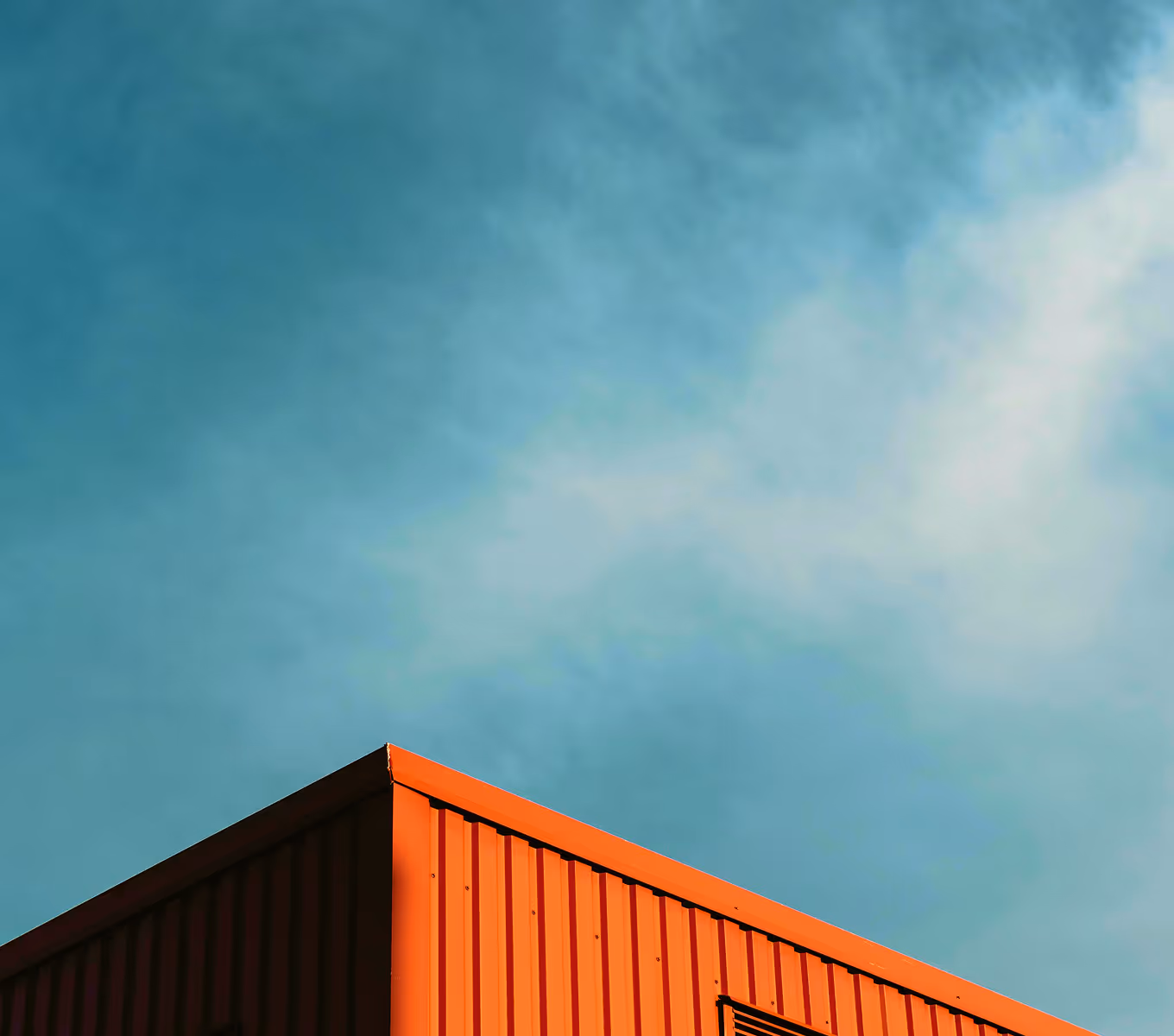 Corner of a red corrugated metal roof against a blue sky with light clouds.