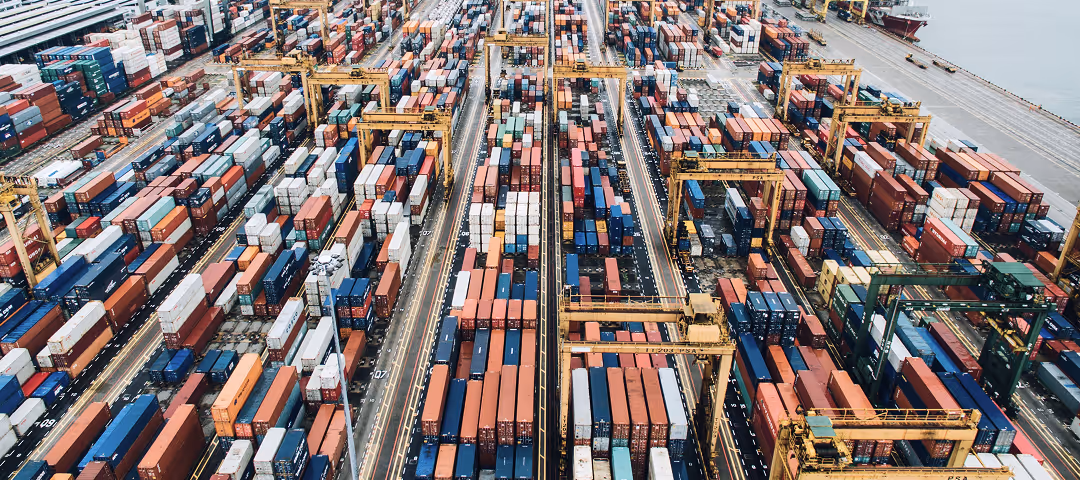 Aerial view of a busy shipping port with numerous colorful shipping containers and yellow cranes arranged in rows.