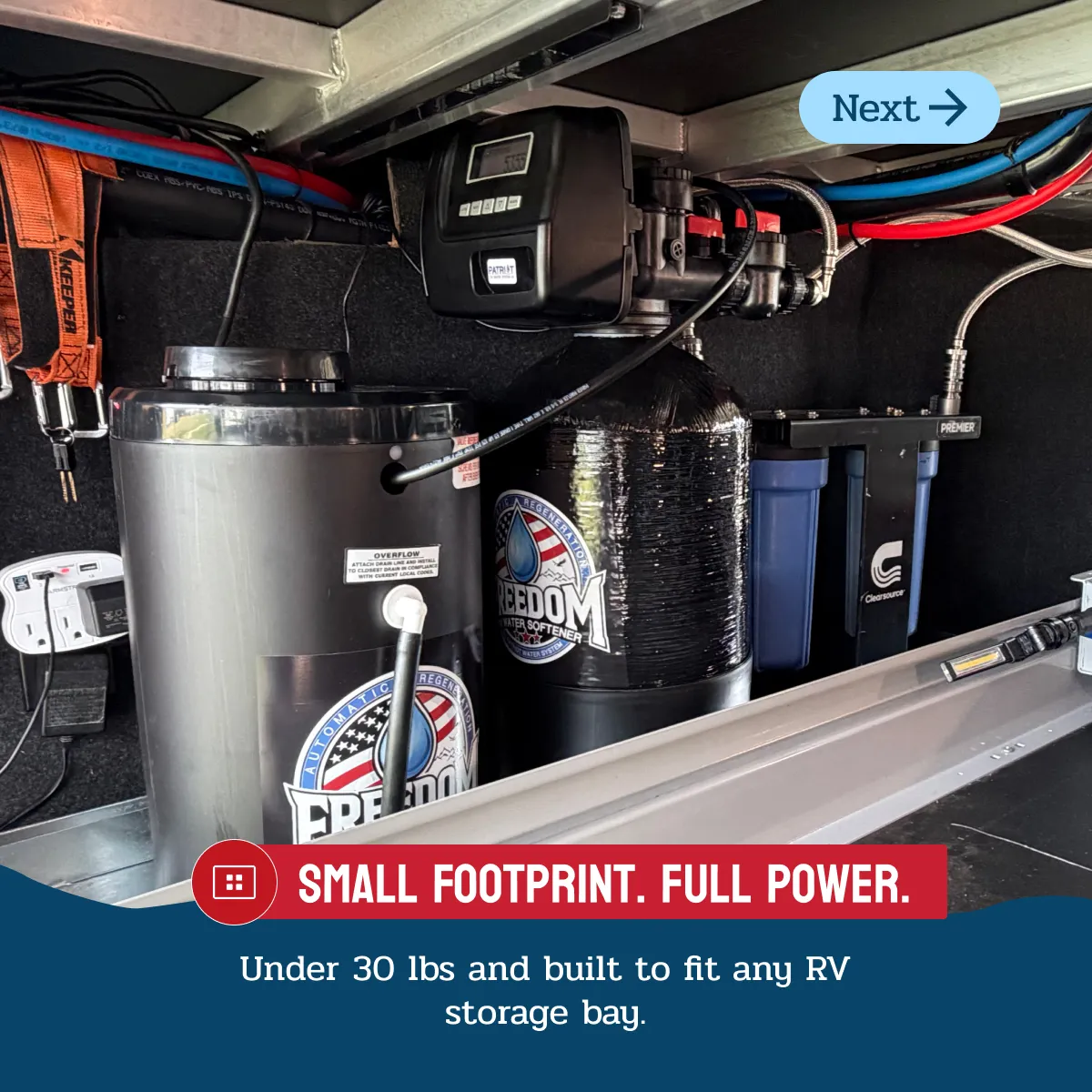 Compact water softener system installed in an RV storage bay with hoses and electrical outlets.