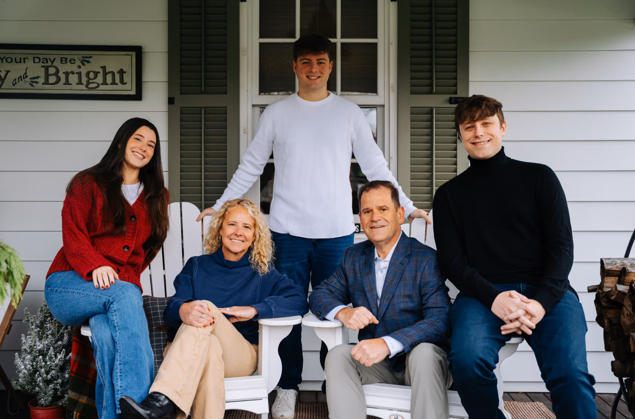 Five people smiling on a porch; two women and a man seated, two young men standing behind in front of a door.