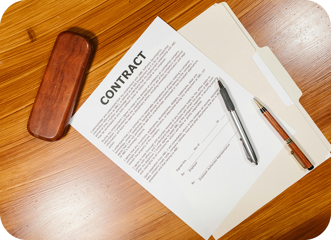 Dokument umowy na biurku z dwoma długopisami i teczką na drewnianym stole.