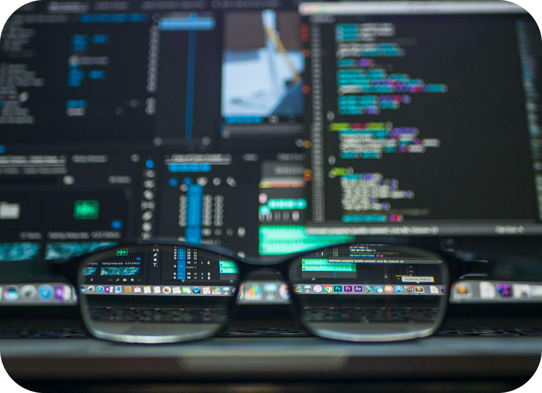 Widok na ekran laptopa z kodem i aplikacjami wyraźnie widoczny przez szkła okularów.