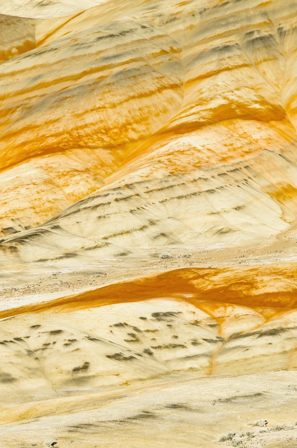 Undulating hills with layers of yellow, orange, and beige rock, featuring streaks of dark gray and black patterns.