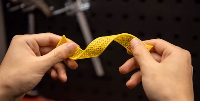 Two hands twisting a flexible yellow perforated strip against a dark background.