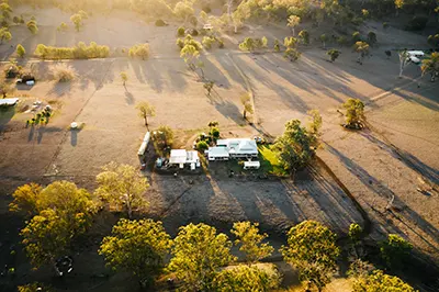 Aerial view of an outback farm. Low sun is casting shadows of the tress and building.