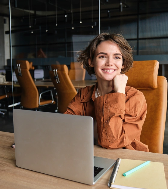 Girl in orange sweater smiling in front of computer