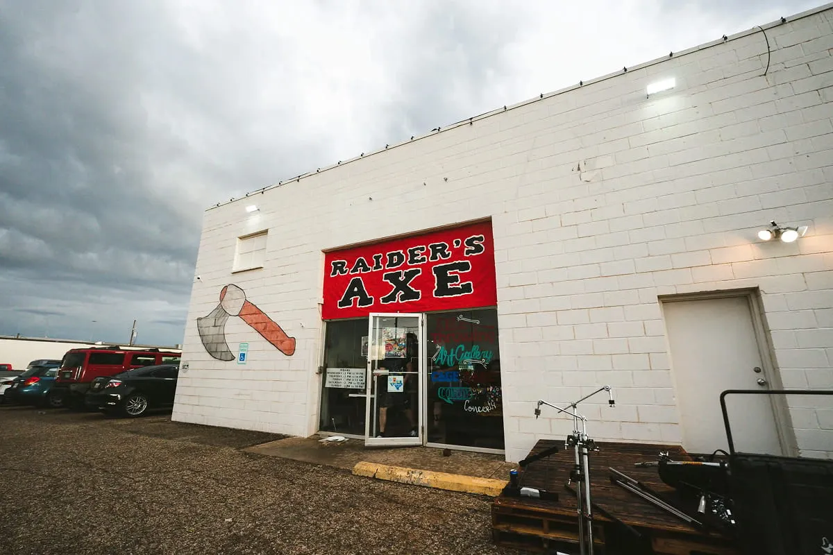 White warehouse building exterior with a glass entrance door and red sign under an overcast sky.