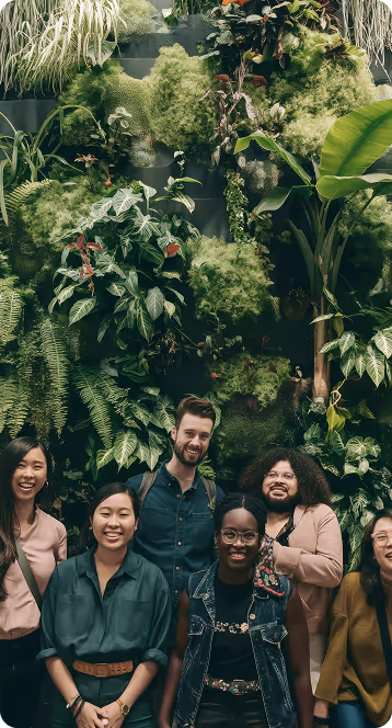 Group of diverse smiling people standing in front of a lush vertical garden wall with various green plants.