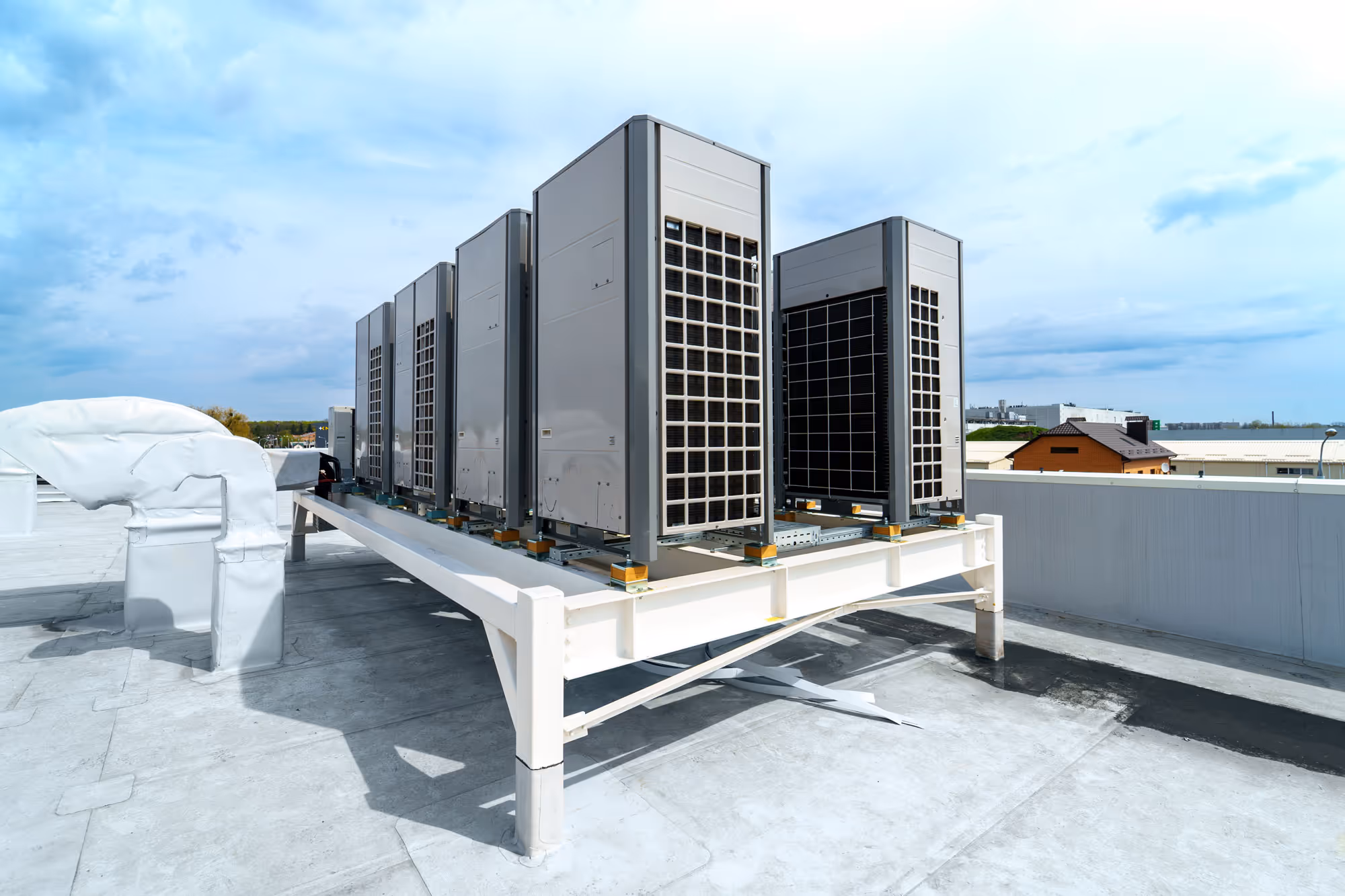 Système de climatisation industriel installé sur le toit d'un bâtiment, composé de plusieurs unités de ventilation grises alignées sur une structure métallique blanche, avec un ciel bleu en arrière-plan.