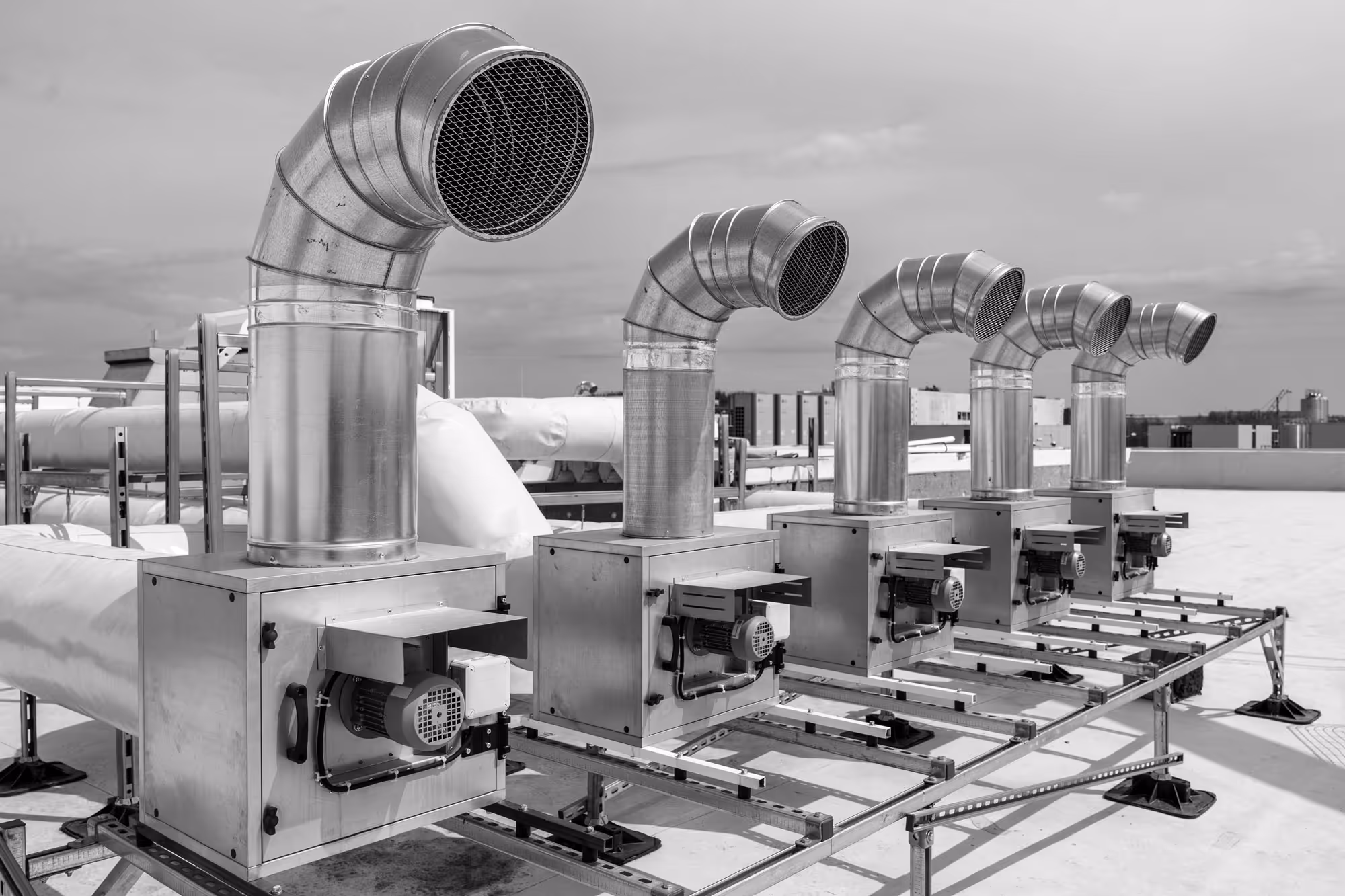 Système industriel de ventilation et climatisation avec cinq unités métalliques alignées sur un toit, chacune équipée d'un conduit d'air incurvé vers le haut.