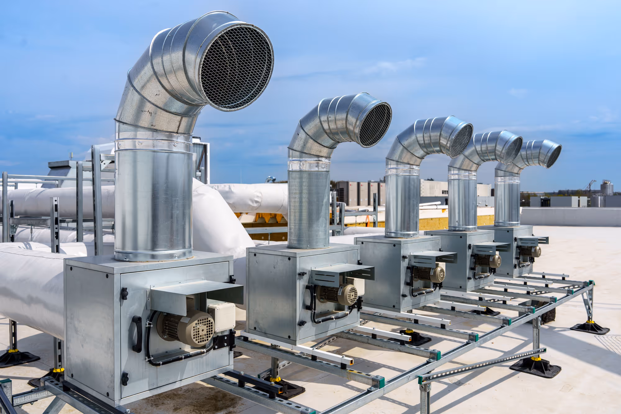 Système de ventilation industriel composé de cinq unités métalliques alignées sur un toit, chacune avec un grand conduit d'aération incurvé vers le haut.
