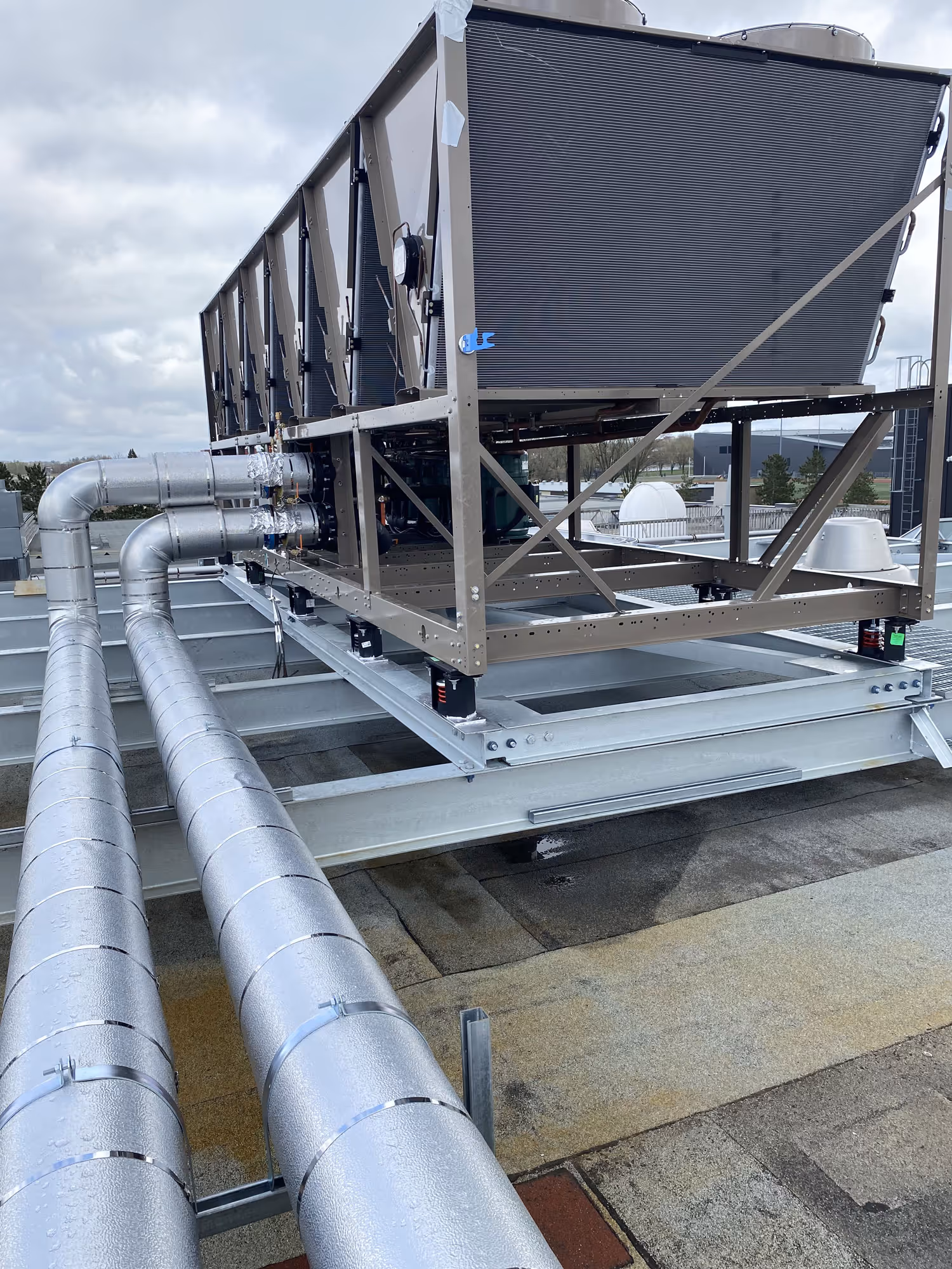 Grande unité de climatisation industrielle sur un toit avec deux grands conduits d'air métalliques connectés, ciel nuageux en arrière-plan.