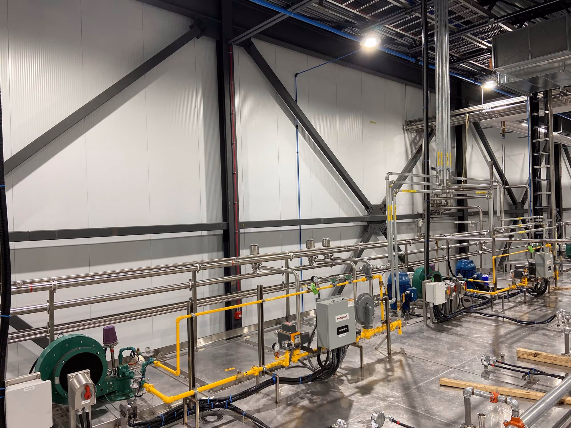 Installation industrielle avec tuyaux métalliques et jaunes alignés au sol dans un grand espace de production éclairé, avec des moteurs et équipements techniques visibles.