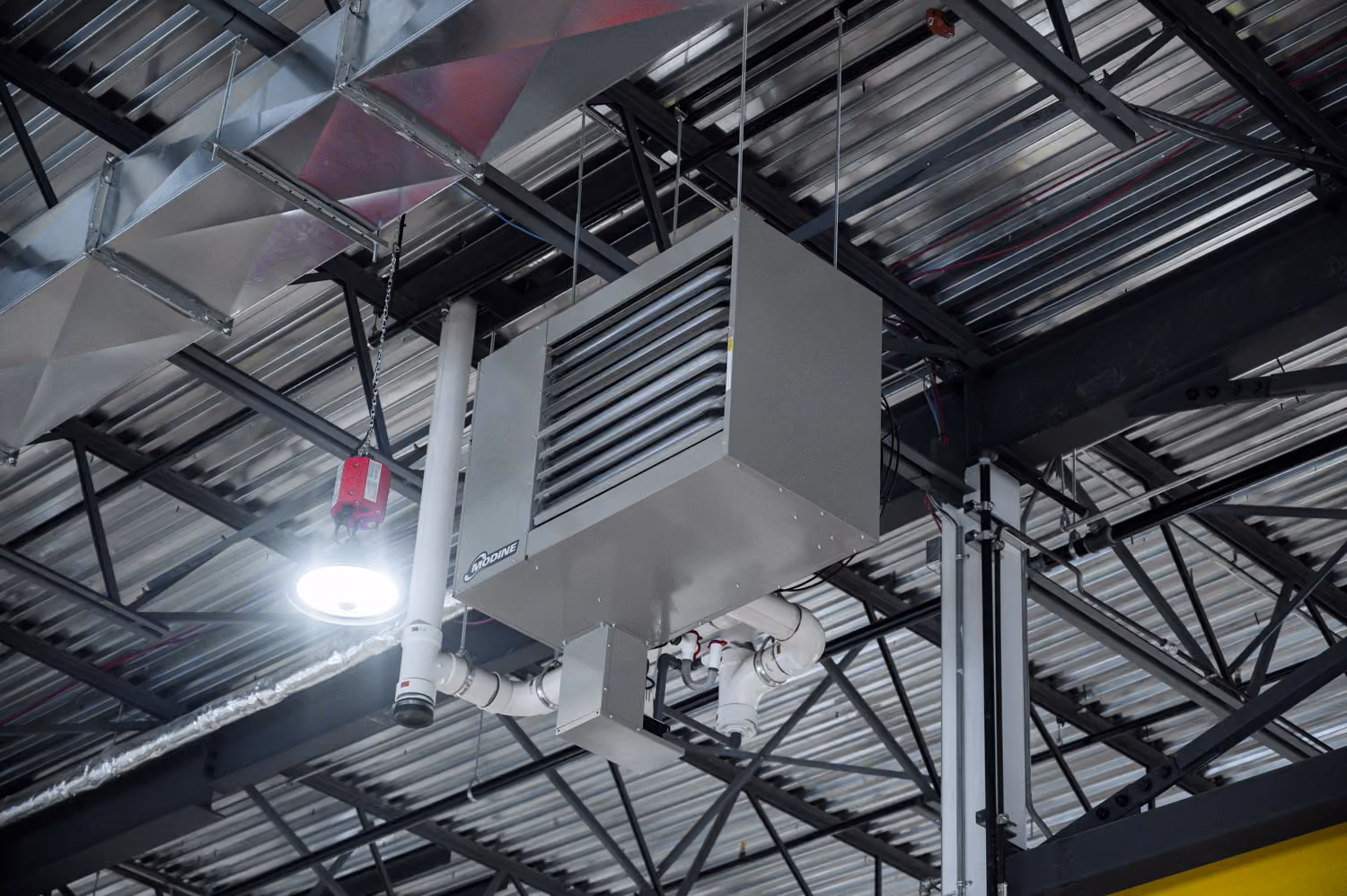 Un système de chauffage suspendu au plafond d'un bâtiment industriel avec des conduits métalliques et une lampe ronde visible à proximité.
