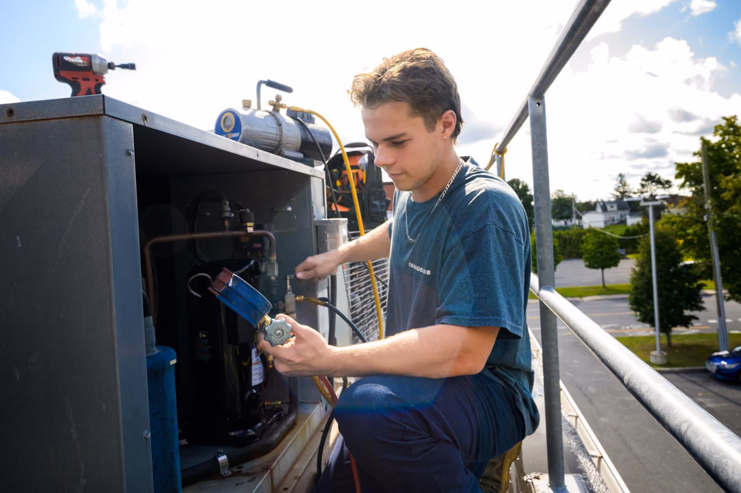 Un technicien travaille sur une unité de climatisation extérieure sur un toit, tenant un manomètre de pression pour vérifier le système.