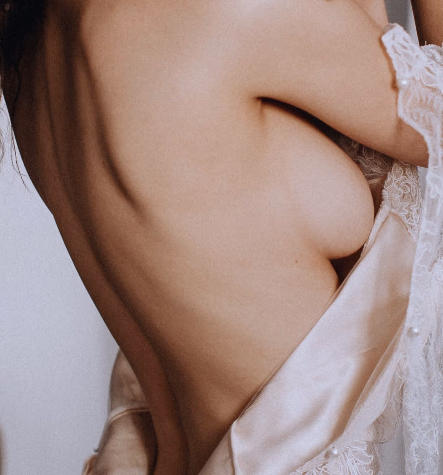 Close-up of a bare back and side of a woman wearing a lace-trimmed silk garment.