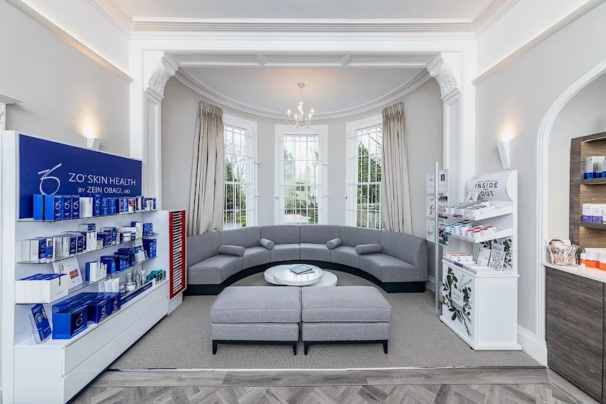 Bright waiting area with curved gray sofa, round white table, ottomans, and skincare product displays.