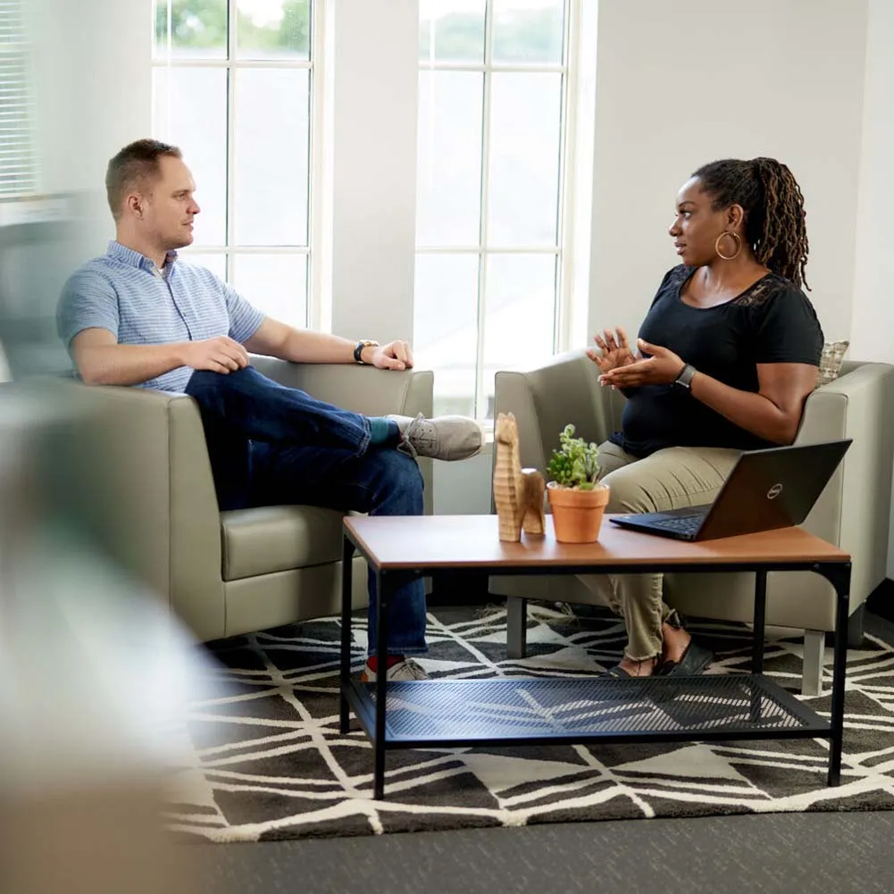A man and a woman sitting in chairs talking.