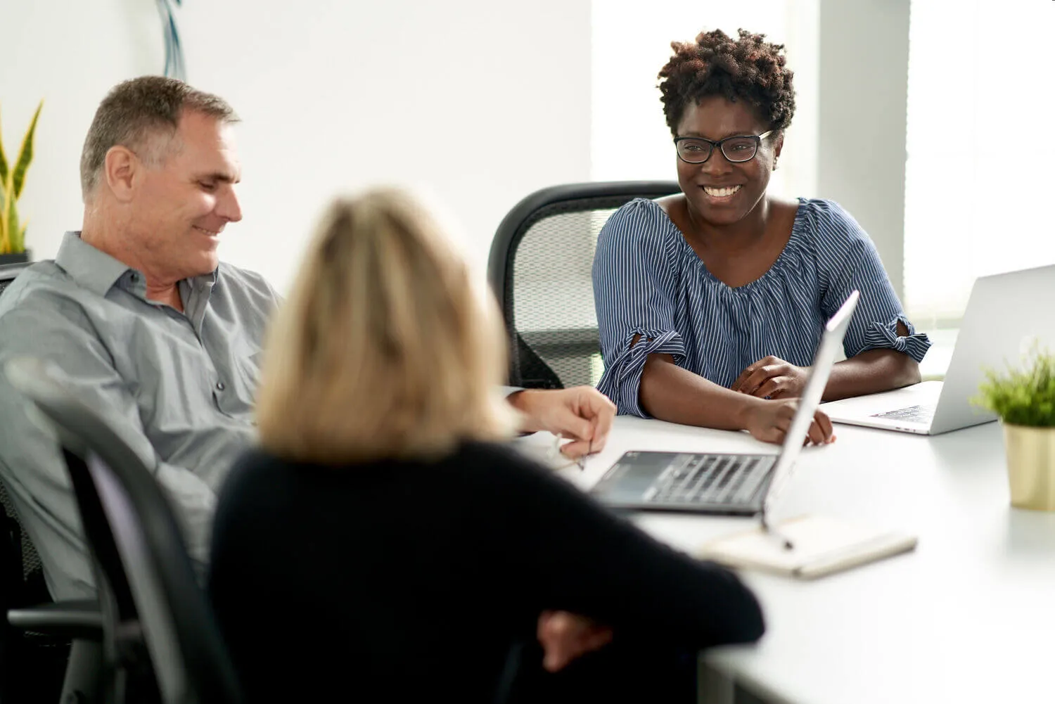 A man and woman sitting at a table with a laptop.