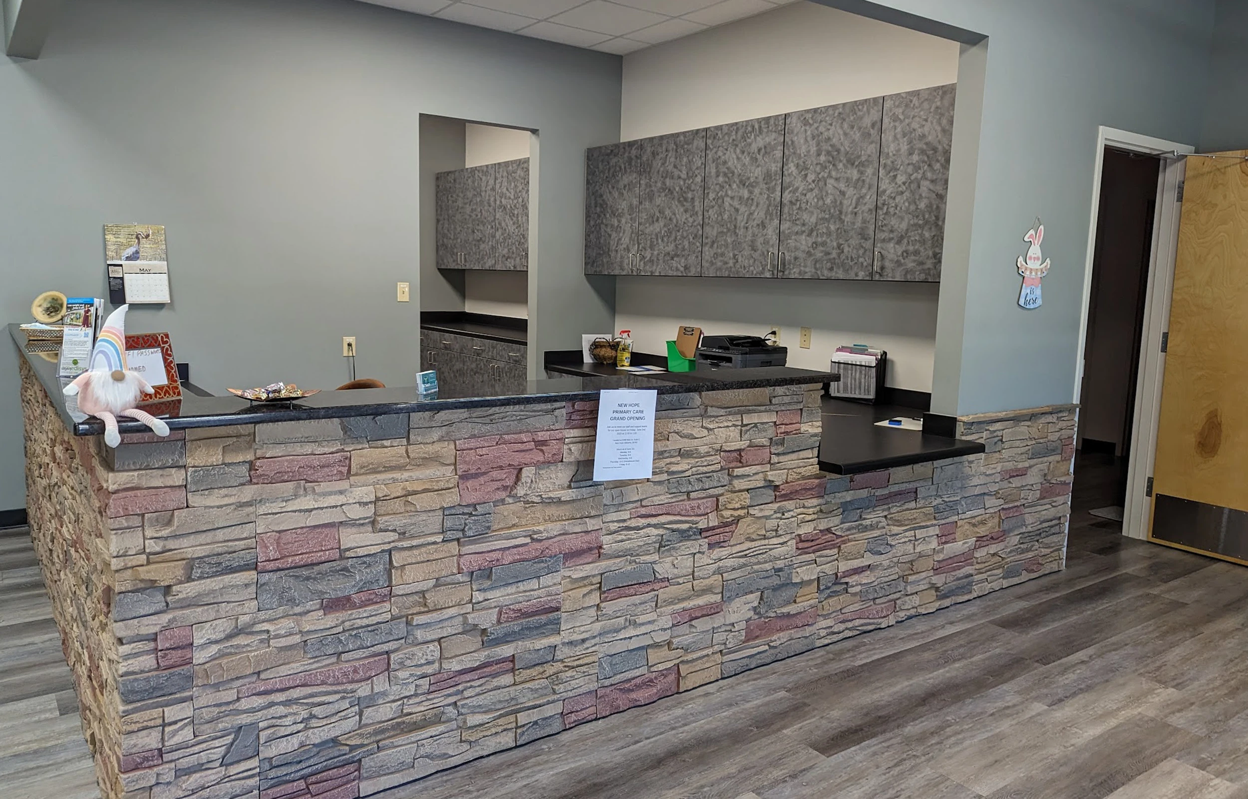 Reception desk with stone facade in an office, decorated with a stuffed gnome and a sign announcing a grand opening.