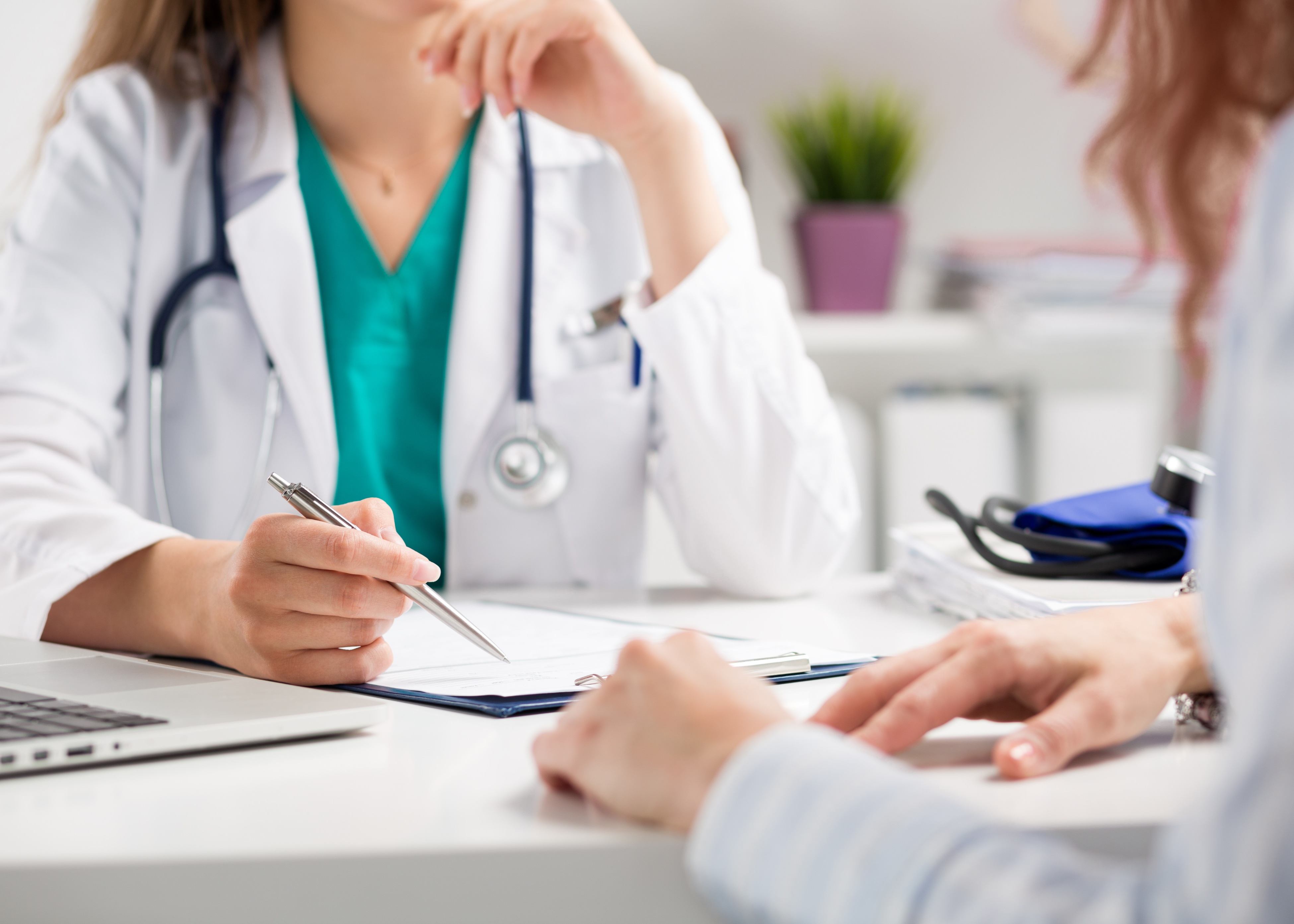 Doctor in white coat holding a pen and reviewing a medical chart with a patient.