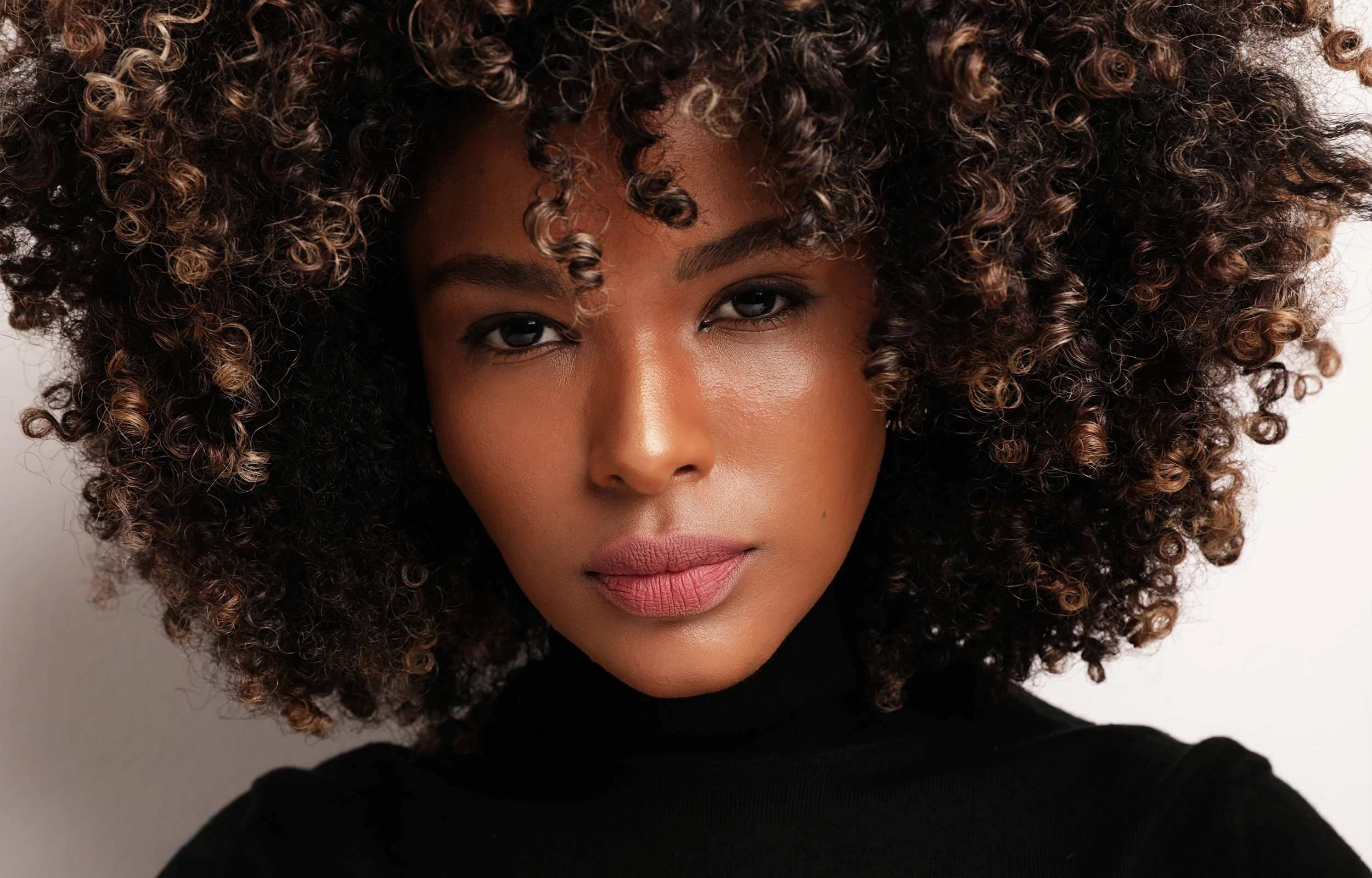 Close-up of a woman with voluminous curly hair and natural makeup wearing a black turtleneck.