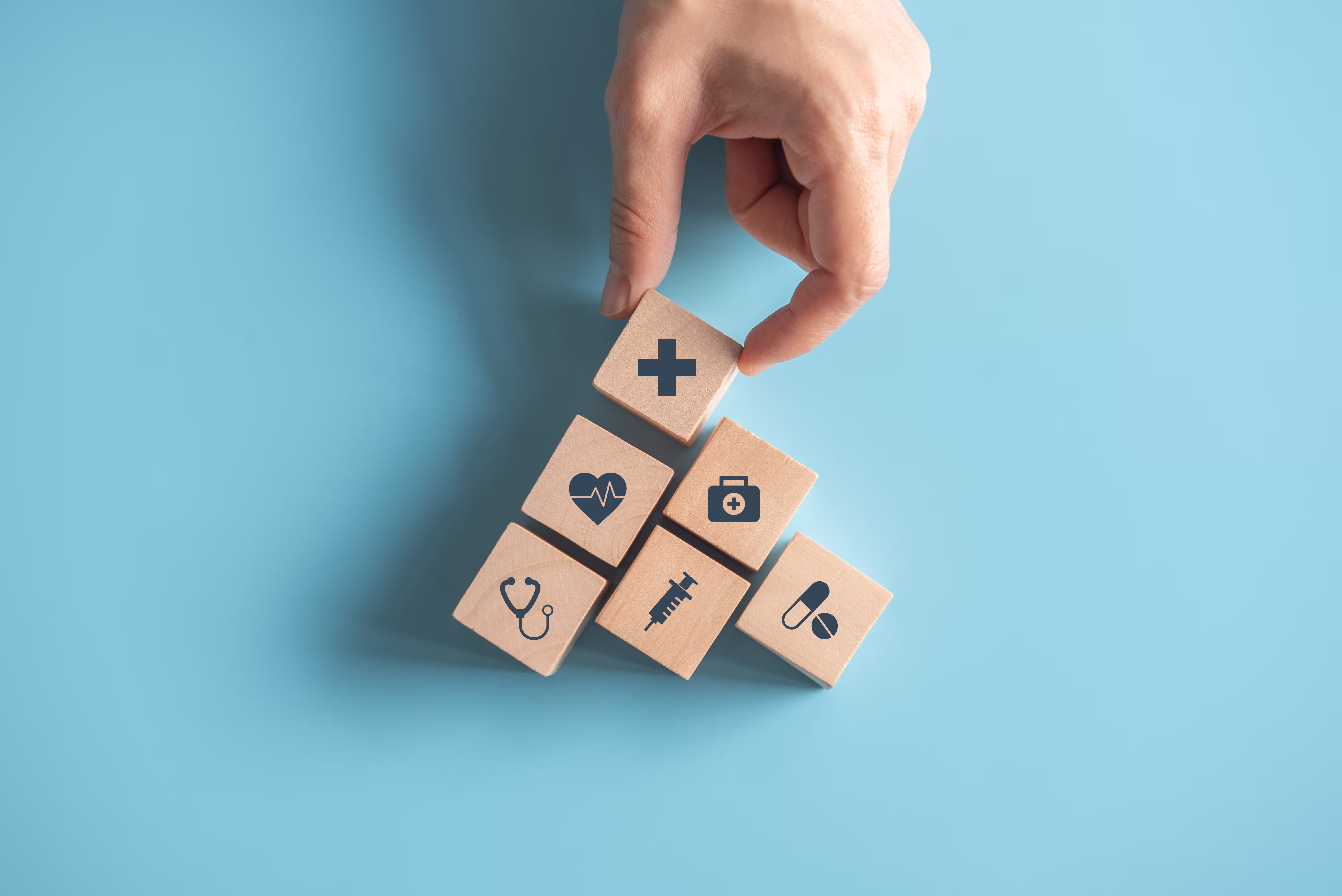 Hand stacking wooden blocks with health-related icons on a blue background.