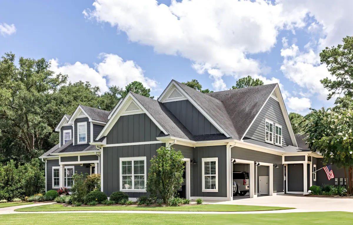 Exterior view of a large gray suburban house with white trim, multiple gables, and an open garage under a partly cloudy sky.