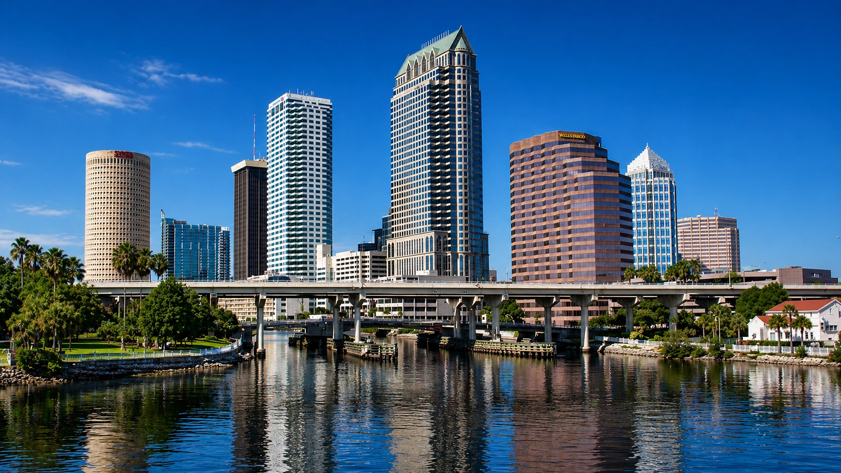Clear blue sky above city skyline with tall buildings reflected in a calm river.