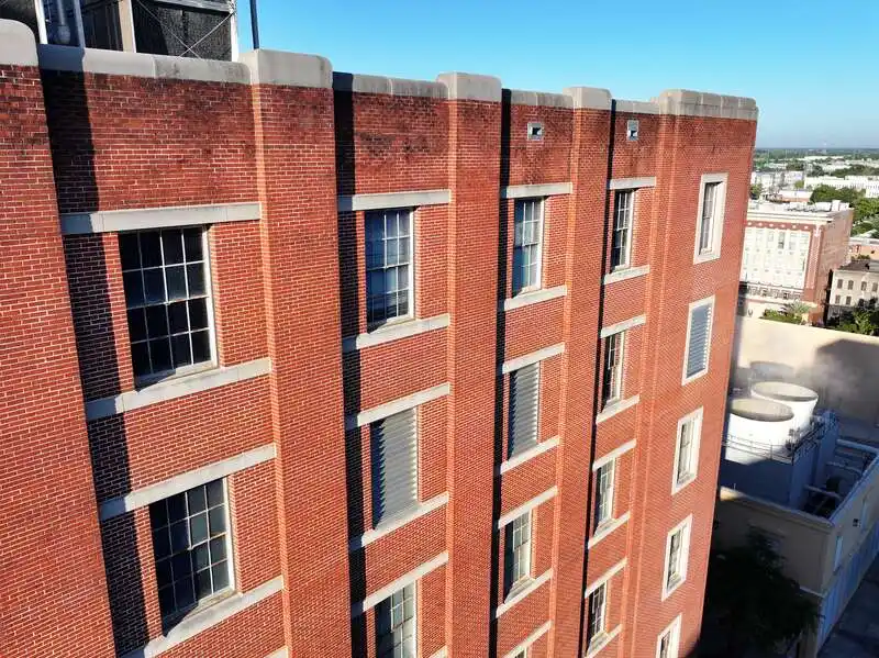 Red brick building with rectangular windows under bright blue sky in an urban area.