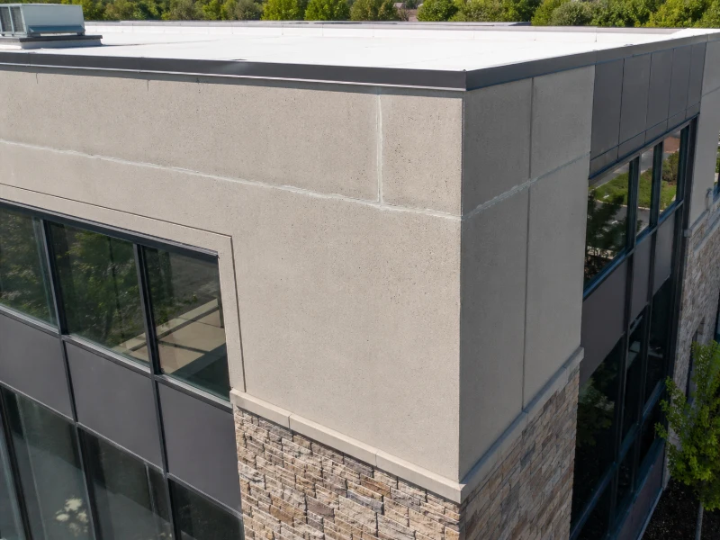 Corner of a modern building with beige concrete and stone facade, and reflective glass windows.