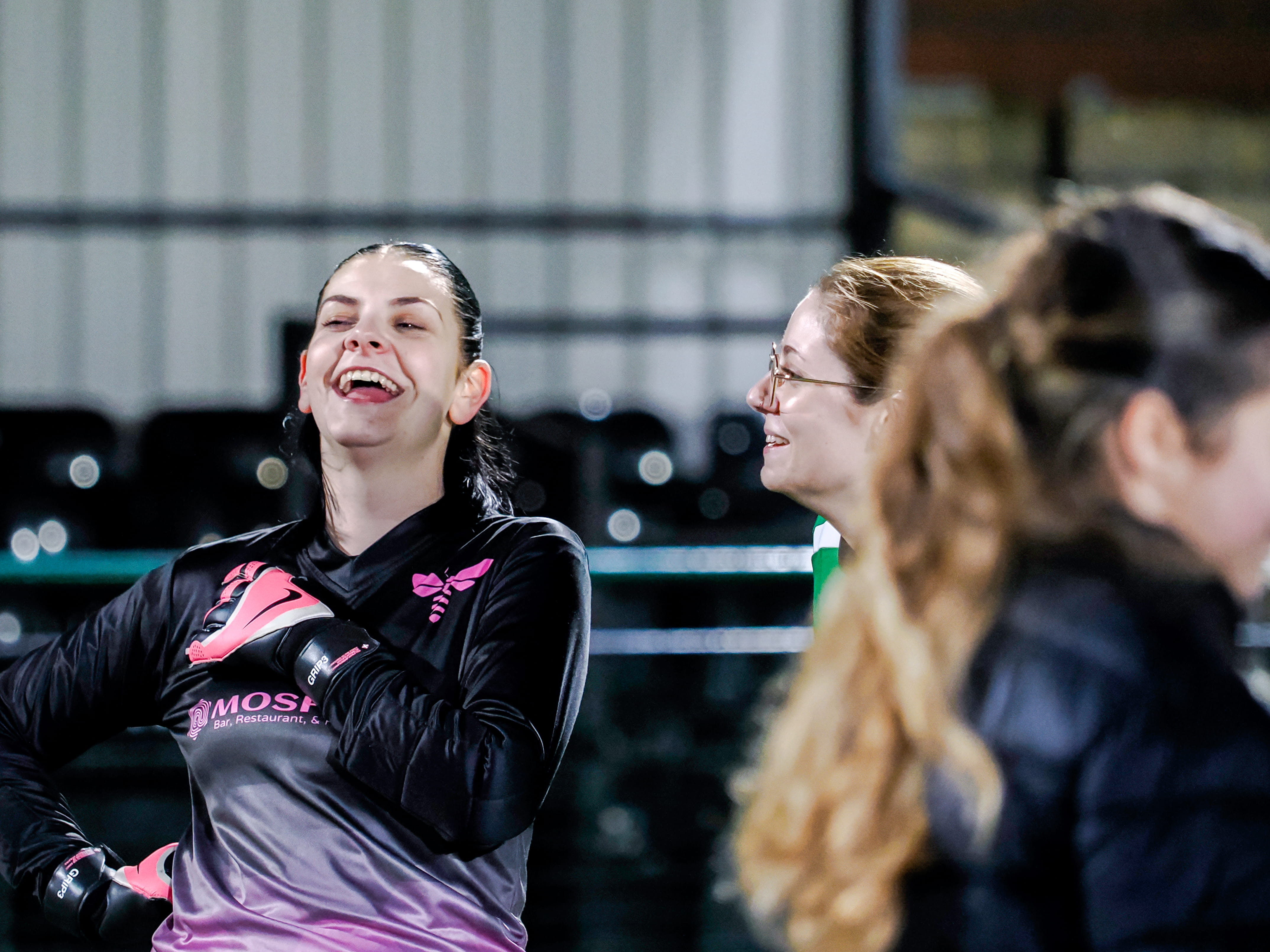A female goalkeeper laughing and conversing with two teammates on the field.