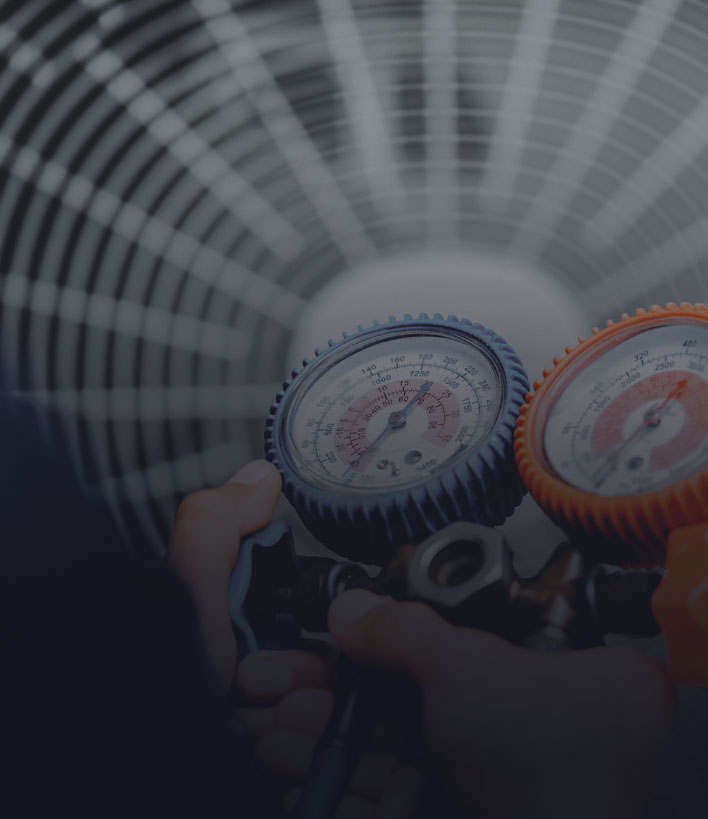 Hands holding HVAC pressure gauges in front of a fan vent.