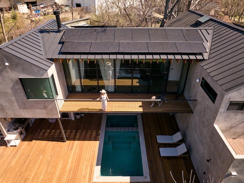 Modern house with a wooden deck, small rectangular pool, and roof mounted solar panels.