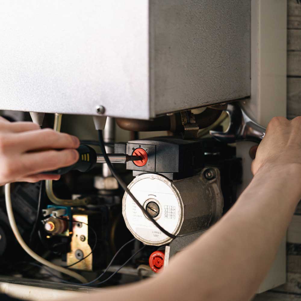 Hands using a screwdriver and wrench to repair or adjust a mechanical component inside a boiler or heating system.
