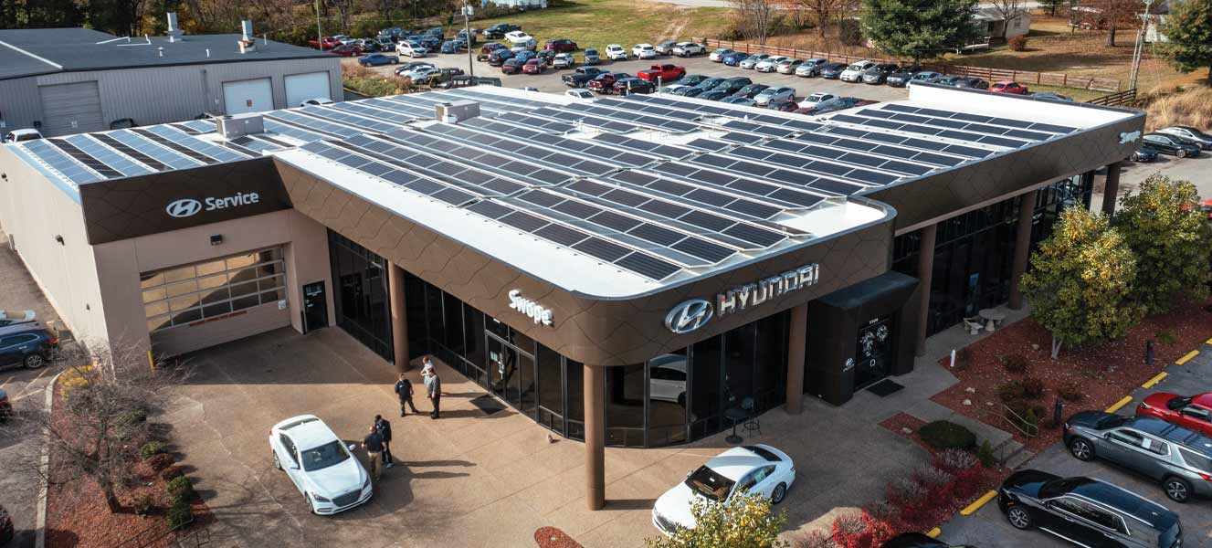 Aerial view of a Hyundai car dealership and service center with solar panels installed by Freedom Power's commercial team covering the roof and several cars parked outside.