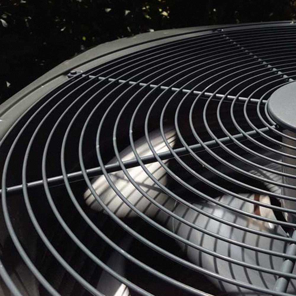 Close-up of a metal fan grille covering the blades of an outdoor air conditioning unit.