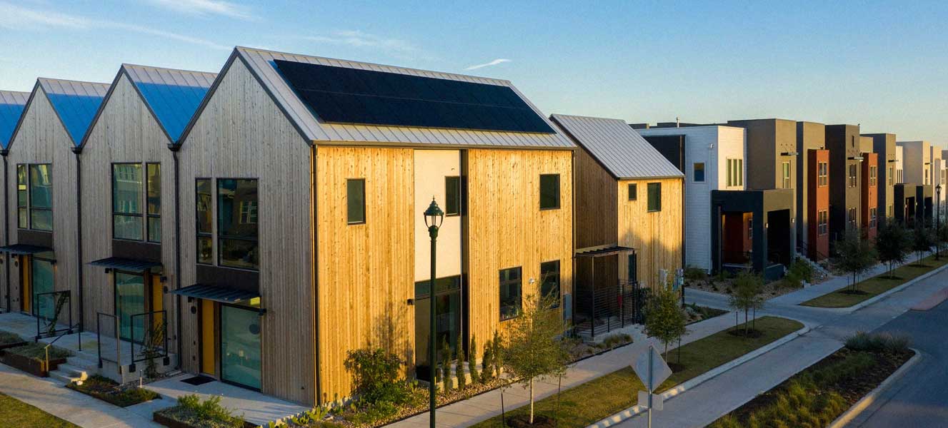 Row of modern townhouses with wooden and steel facades, solar panels on rooftops, and landscaped sidewalks.