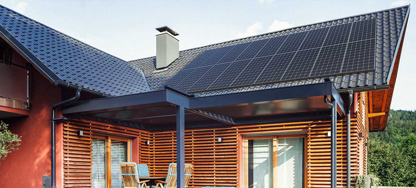 Modern house with wooden exterior and solar panels installed on a tiled roof under a clear sky.