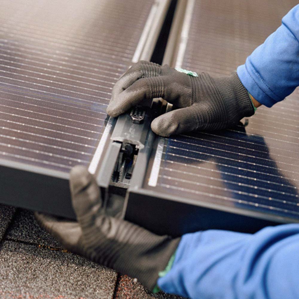 Hands wearing black gloves installing or connecting two solar panels on a rooftop surface.