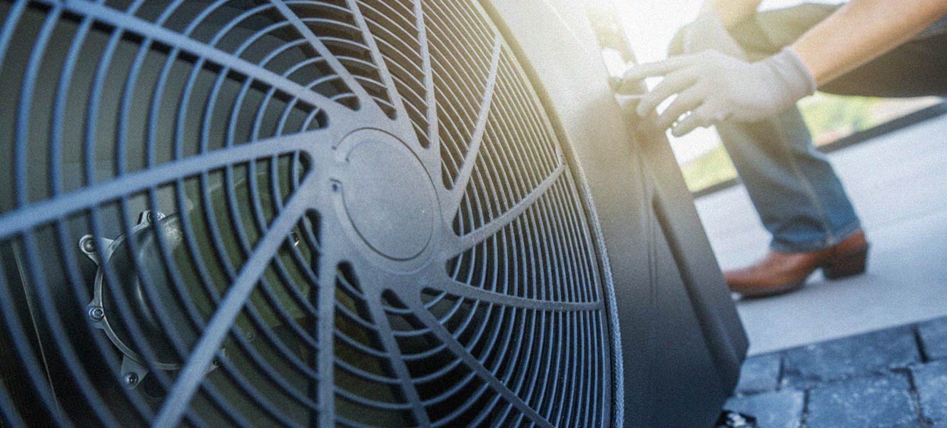 Technician wearing gloves performing maintenance on an outdoor HVAC unit's fan.