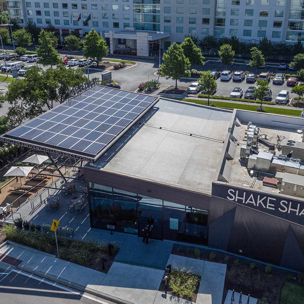 Aerial view of a Shake Shack restaurant with solar panels installed by Freedom Power's commercial team on the roof and outdoor seating under umbrellas.