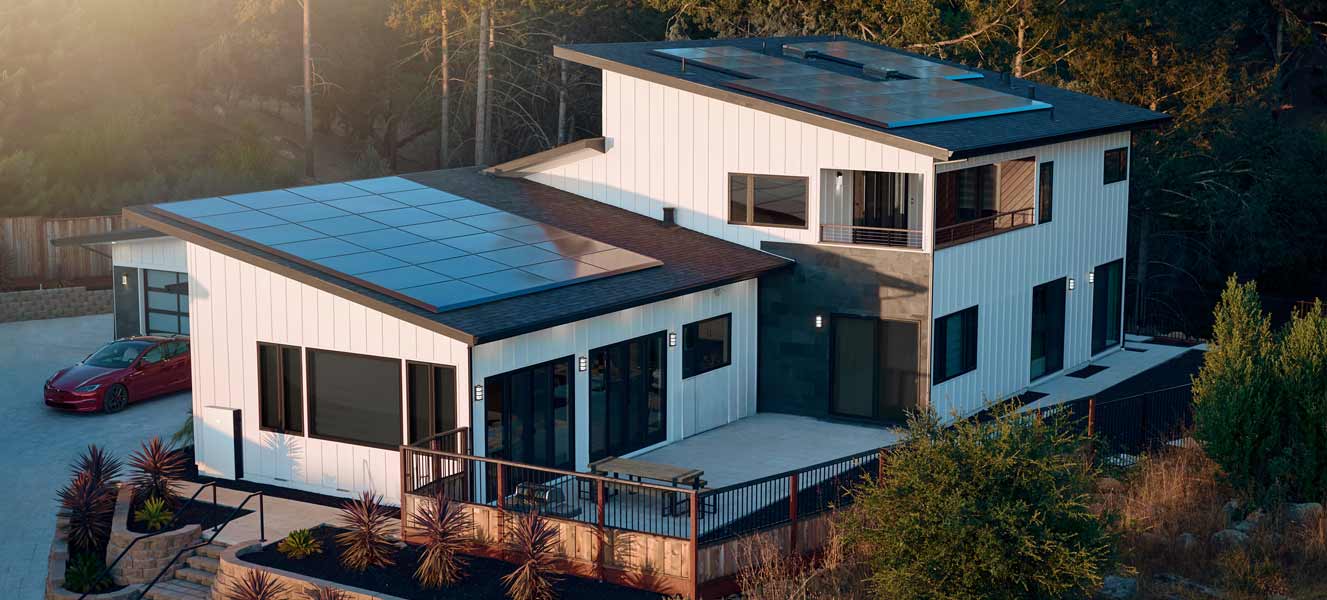 Sunrise creeping over a tree line onto a modern home outfitted with solar panels along its rooftop installed by Freedom Power