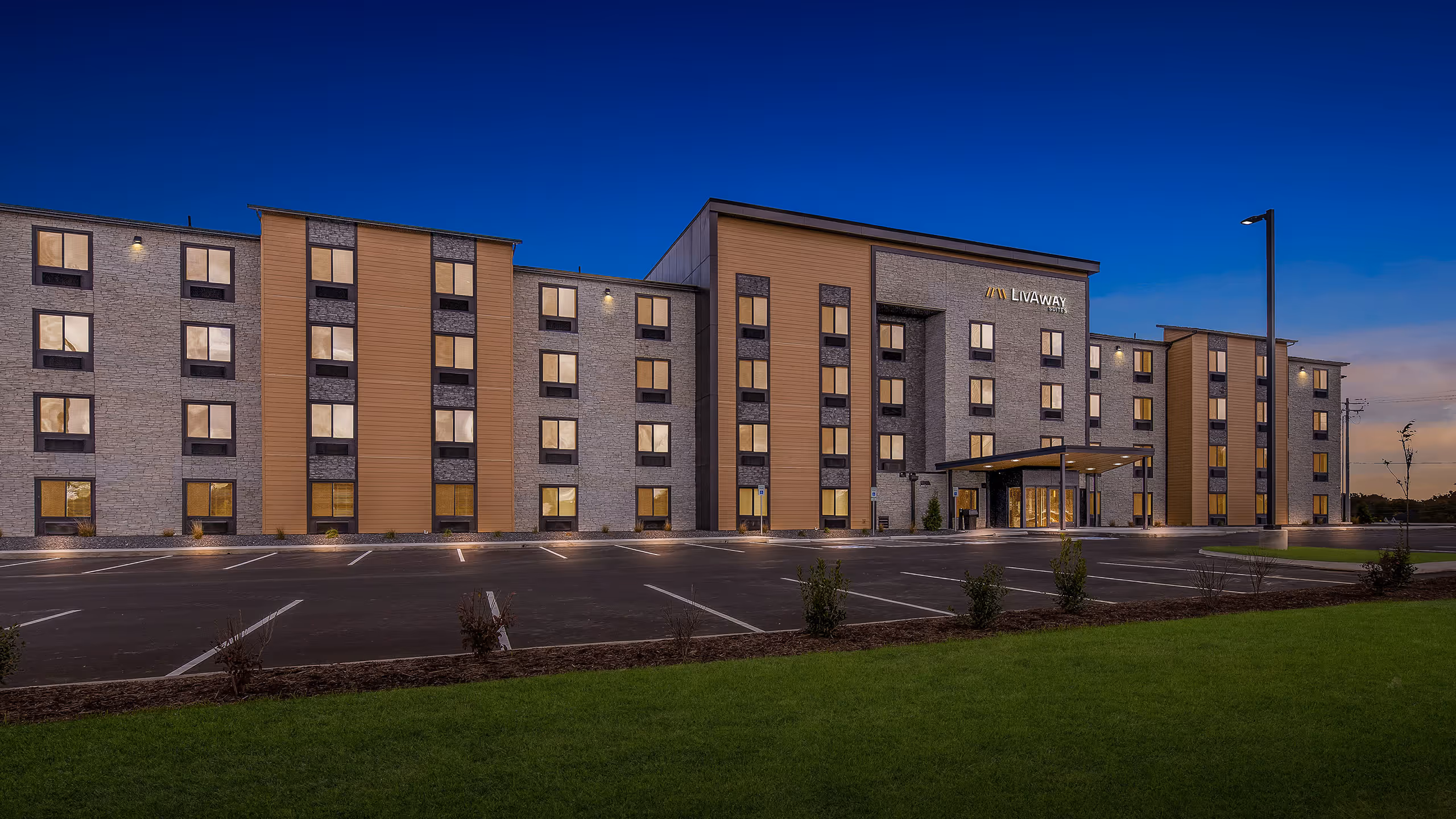 Four-story Livaway hotel building with illuminated windows and empty parking lot at twilight.