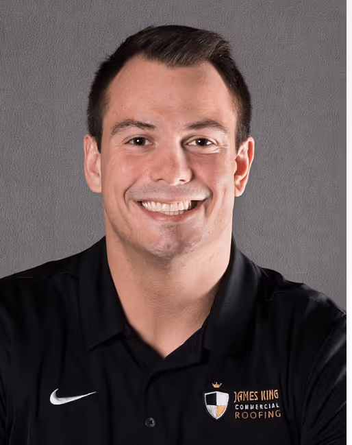 Smiling man wearing a black polo shirt with James King Commercial Roofing logo and a white Nike swoosh on a gray background.
