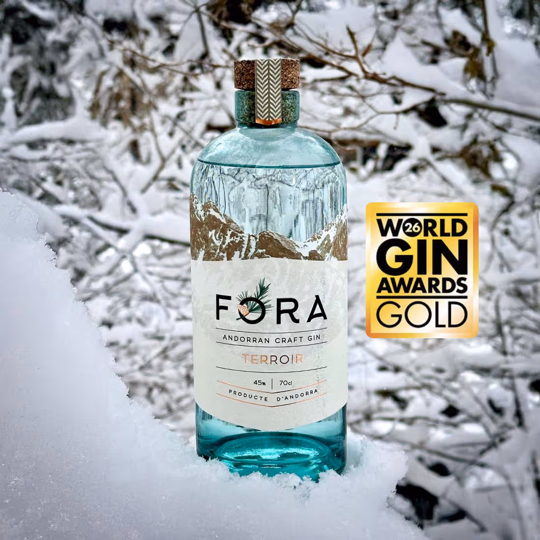 Ampolla de gin artesanal FORA Terroir d'Andorra amb un premi d'or al World Gin Awards, sobre neu i un fons de branques nevades.
